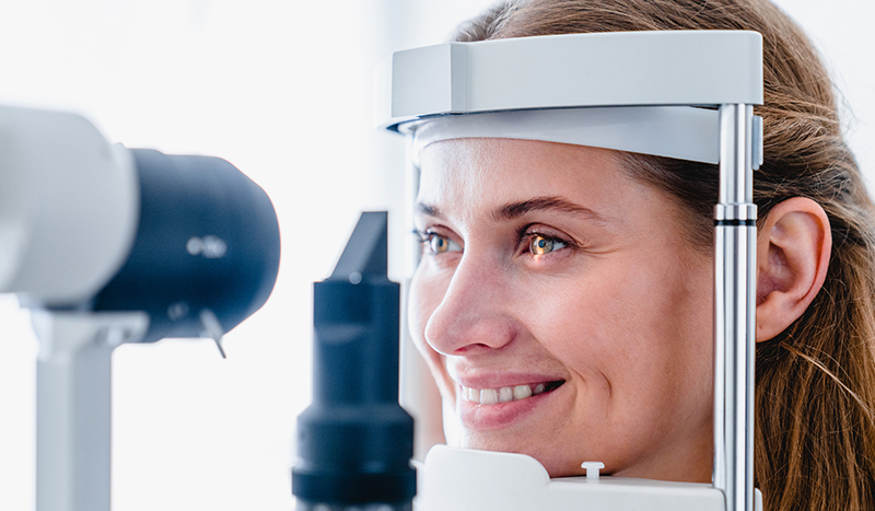 Close up photo of a smiling young woman patient during ophthalmic sight examination Eye Exams in Snowmass Village & Lone Tree, CO